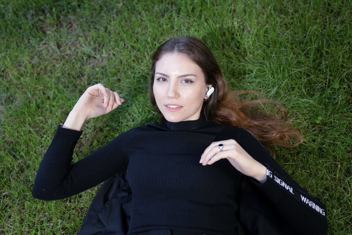 Photo of woman lying on grass and wearing Natura Umana's HumanPods earbuds.